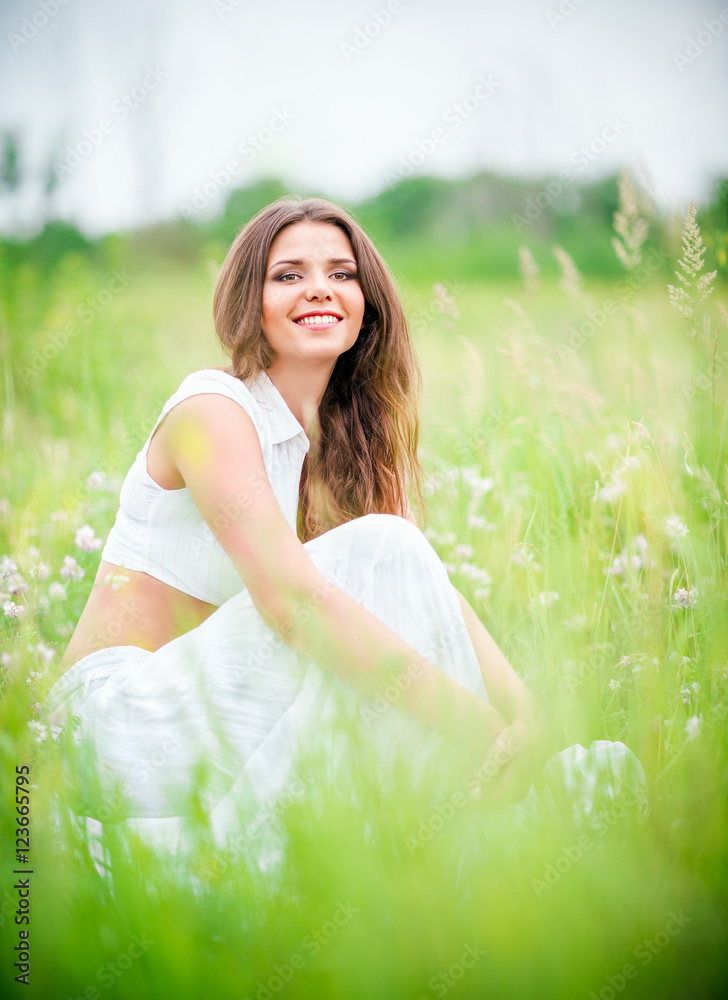 Happy smiling beautiful young woman sitting among grass and flowers Happy smiling beautiful young woman sitting among grass and flowers