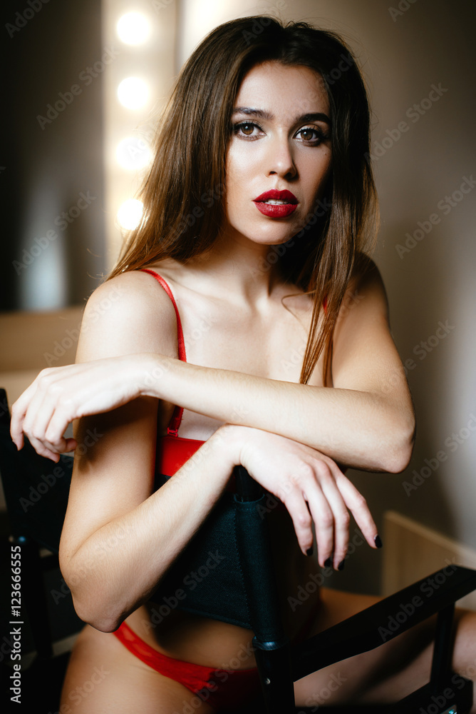 Soft focus. Beautiful sexy brunette girl in the dressing room on the background lights. Dressed in a sexy red lace underwear. Posing outside chairs Soft focus. Beautiful sexy brunette girl in the dressing room on the background lights. Dressed in a sexy red lace underwear. Posing outside chairs