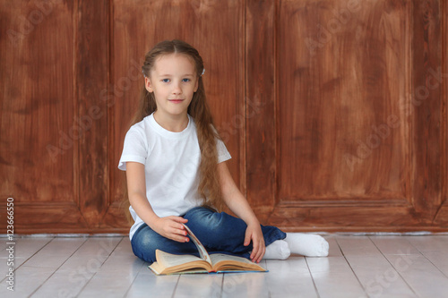 Little girl sitting on the wooden floor and reading book