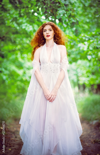 Cute red-haired woman wearing white dress in a garden