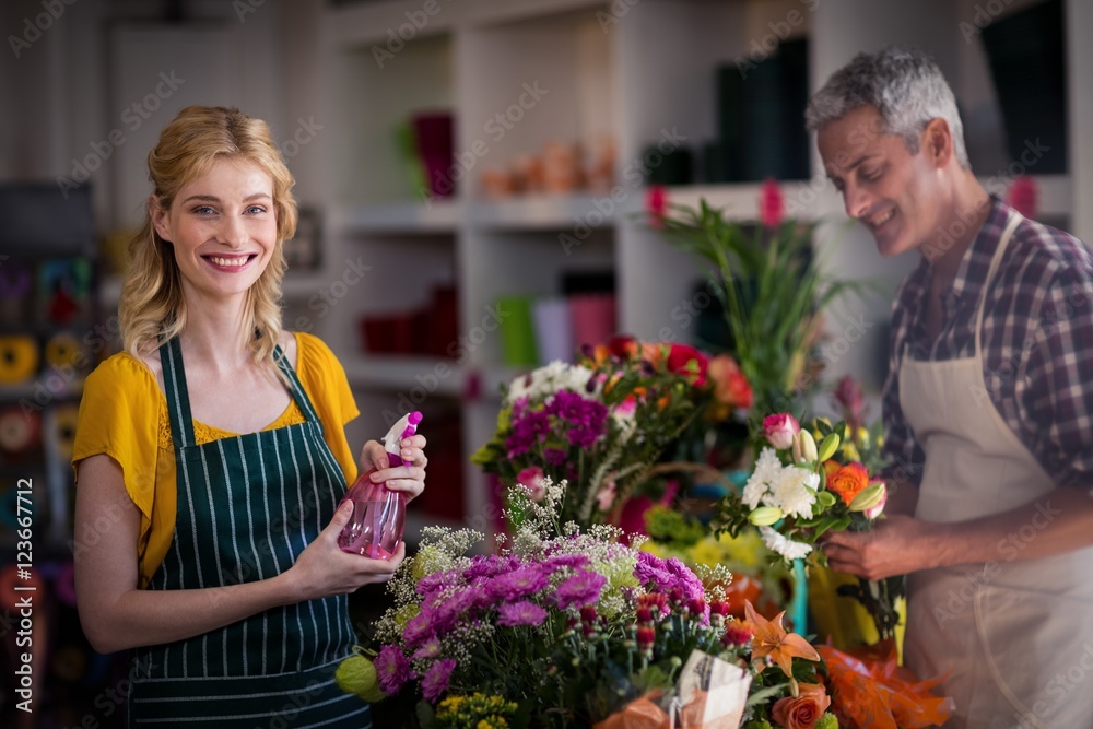 Smiling florist spraying water on flowers in flower shop