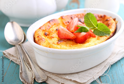 Cottage cheese casserole in white dish decorated with strawberries, on a blue background
