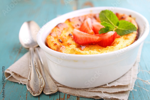 Cottage cheese casserole in white dish decorated with strawberries, on a blue background