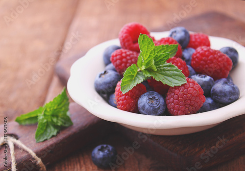 healthy breakfast. raspberries and blueberries in a white bowl on a wooden background.