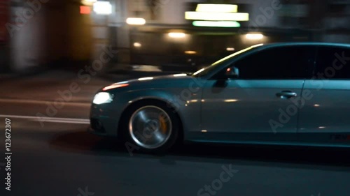 Side shot of a blue car driving in a city street at night
