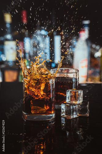 Billede på lærred two glasses of whiskey on a blurred background bar