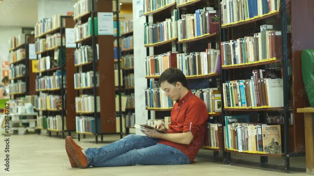 male college student sitting on floor in library, reading book. male college student sitting on floor in library, reading book.