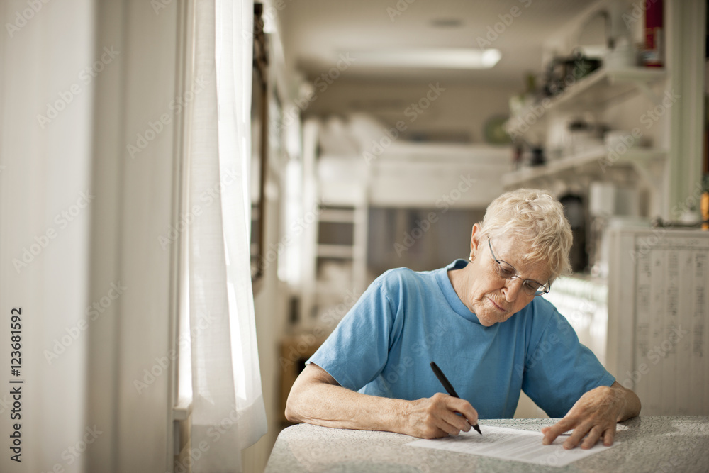 Senior woman writing on paper at kitchen Senior woman writing on paper at kitchen