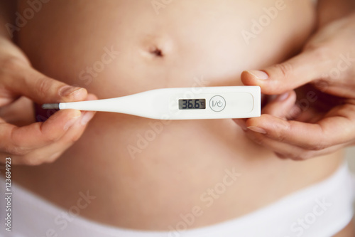Pregnant woman with a thermometer in hands.