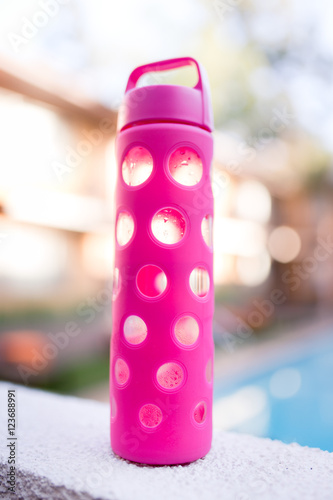 A glass hot pink water bottle is half full of cold water.
