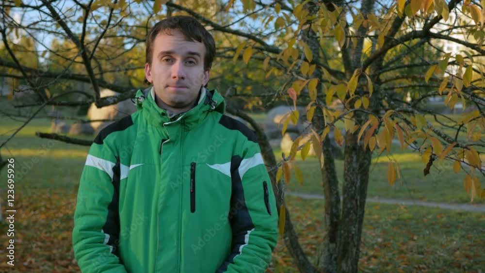 Young handsome man looking into the camera in autumn park. Equip a green sports jacket warm Young handsome man looking into the camera in autumn park. Equip a green sports jacket warm