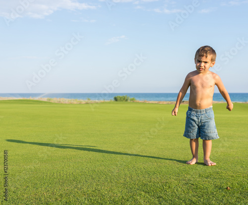 Happy little boy on summer gulf grass terrain having fun and hap