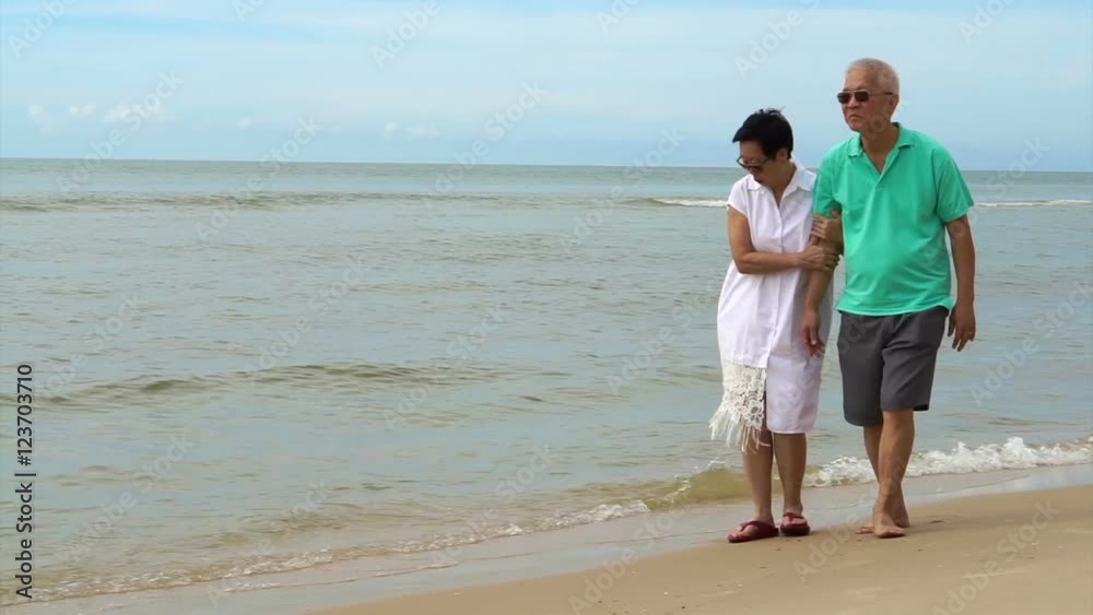 Asian senior couple walking happily by the beach. holding hand and talk with each other Asian senior couple walking happily by the beach. holding hand and talk with each other
