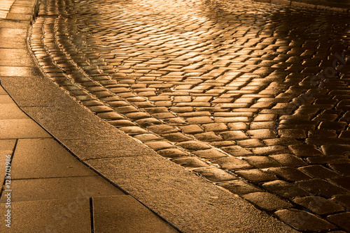 Straßenkurve mit golden glänzendem Kopfsteinpflaster im Regen