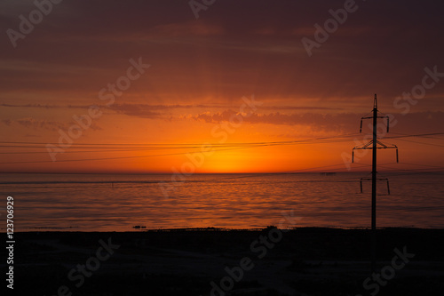 Power lines near the sea in a background of red sunrise light
