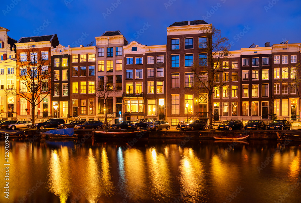 Typical dutch houses over canal with reflections illuminated at night, Amsterdam, Netherlands