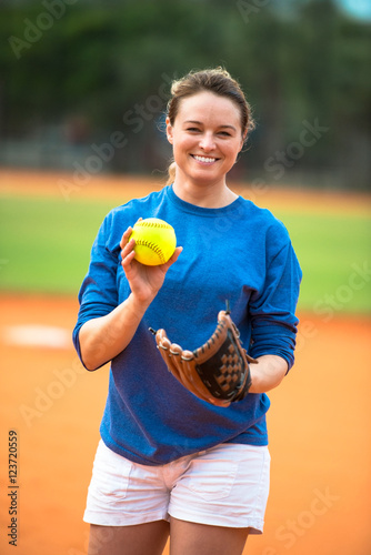 Smiling young woman softball player pitcher with bright fluorescent neon yellow ball in pitching circle