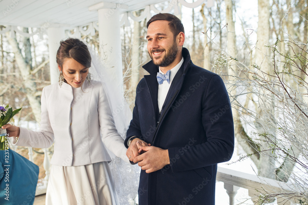 Stunning groom holds bride's hand tightly standing on the porch Stunning groom holds bride's hand tightly standing on the porch