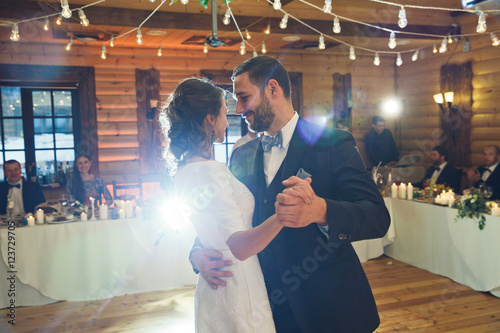 Stylish just married couple dances in the middle of wooden hall