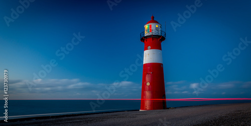 Red lighthouse during sunset on a dike at sea