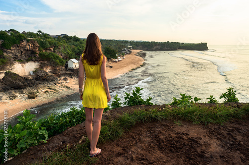 Girl in yellow dress looking forward from the cliff  on Balangan beach. Bali. Indonesia. photo
