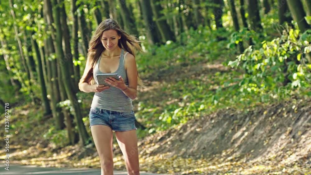 Beautiful girl on rollers and uses the tablet in a summer park Beautiful girl on rollers and uses the tablet in a summer park