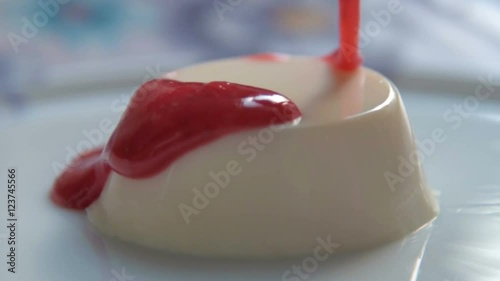 Slow motion close-up shot of pouring panna cotta dessert with strawberry sauce