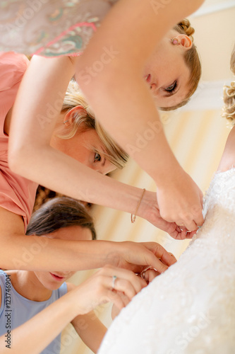 Bridesmaids are helping to the bride with the gown