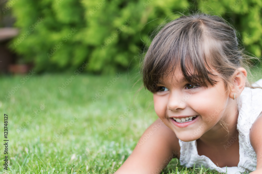 Closeup view of the toothy smiling face of little girl lying on the grass outdoors. Free place for your text is in the left side of the photo. Closeup view of the toothy smiling face of little girl lying on the grass outdoors. Free place for your text is in the left side of the photo.