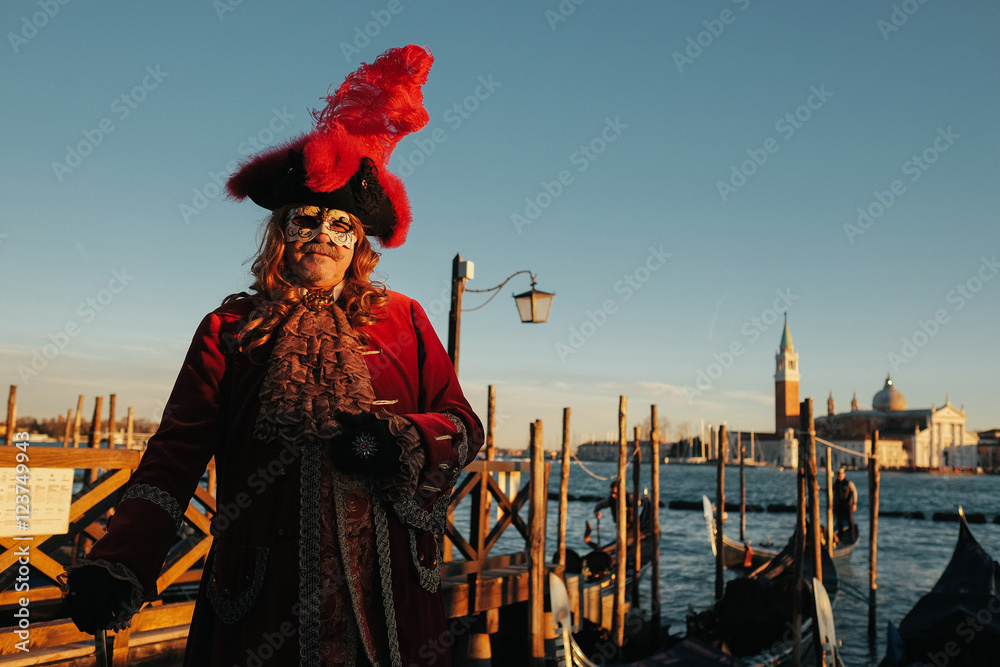 A man in old red Italian suit in a hat with feather stands on th