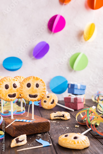 Homemade shortbread smiley cookies with dark chocolate on stick called pie pops. Childrens party background.