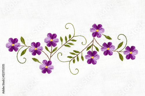 Embroidered satin stitch,melange thread purple flowers with leaves on cotton cloth
