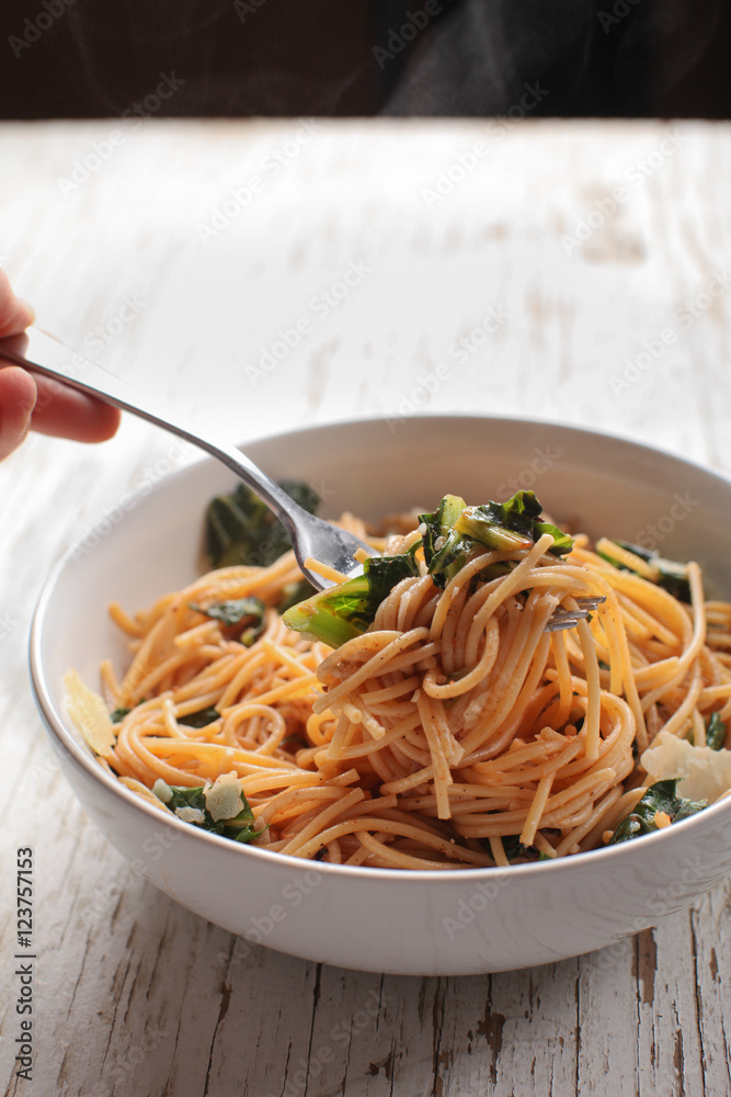 Kale, Tomato and Parmesan pasta dish with hand holding fork