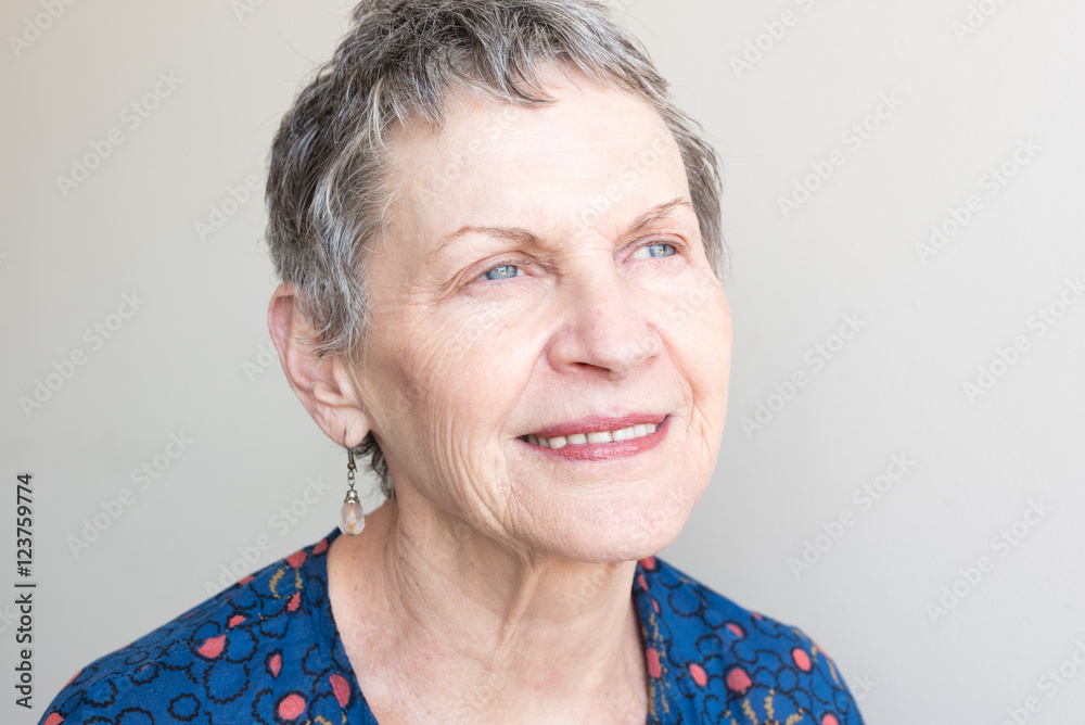 Closeup of older woman in blue top looking up hopefully against neutral background Closeup of older woman in blue top looking up hopefully against neutral background