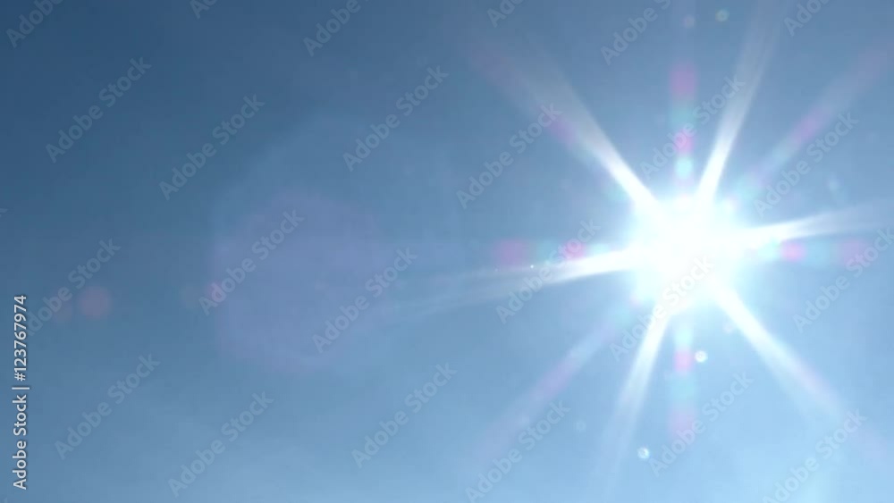Clear blue sky day with bright sun shining and flare as camera pans.