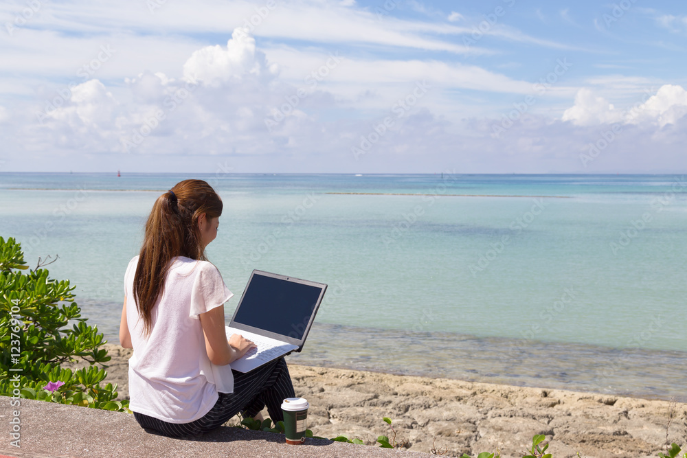 海辺でパソコンを操作する若い女性