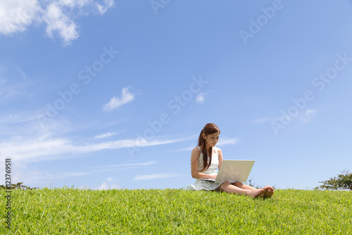 青空の下でパソコンを操作する若い女性
