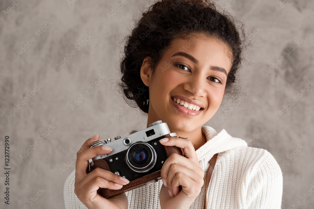 African female photograph smiling, holding camera over beige background. African female photograph smiling, holding camera over beige background.