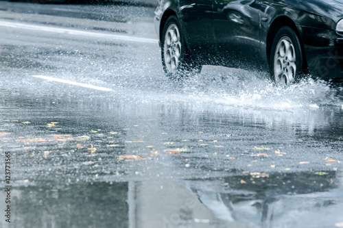 black car driving through rain puddle with splashing water from its wheels