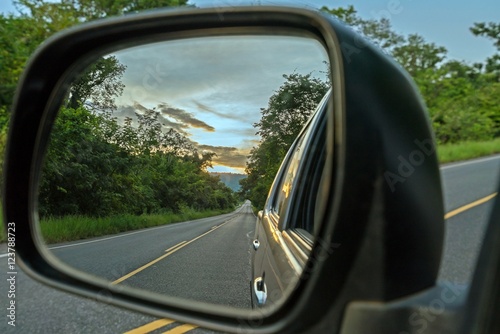  Reflection seen through car side mirror -  two-lane winding road with twilight sky and sunset
