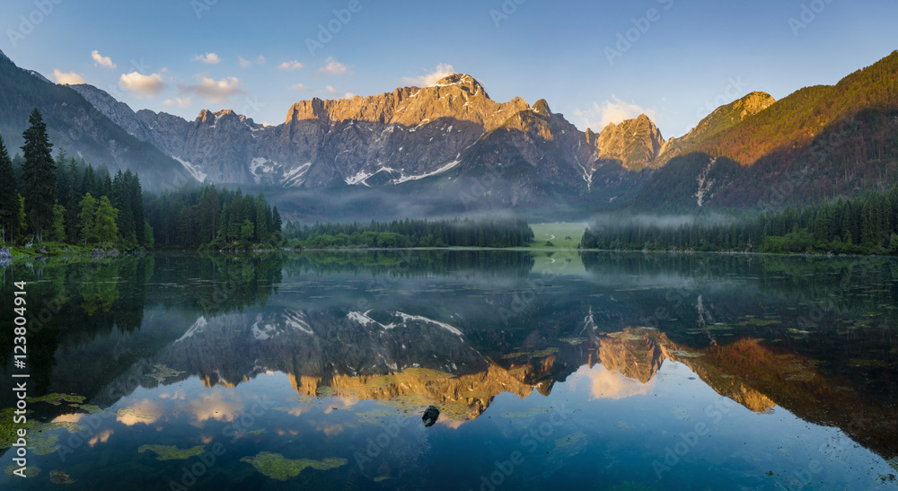reflection of  mountain Mangart in a mountain lake Laghi di Fusine at sunrise, Julian Alps, Italy