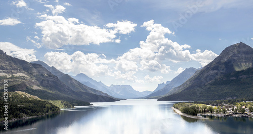 horizontal image of a landscape of a large lake with mountains looming on either side under a bright blue sky with white clouds in the summer time.
