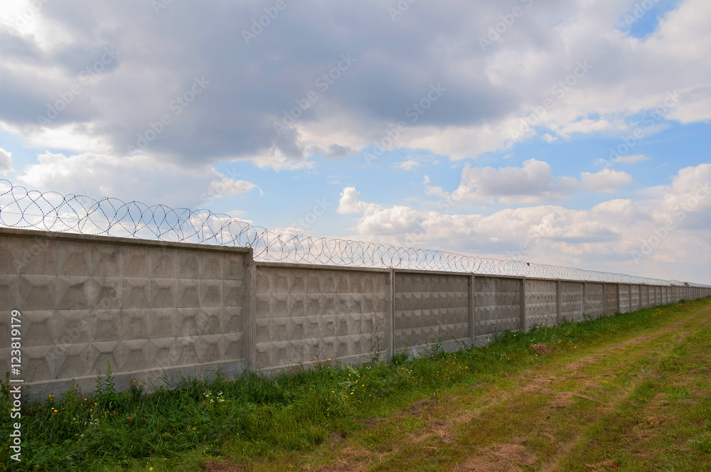 Wall with barbed wire on a background of blue sky. long fence Wall with barbed wire on a background of blue sky. long fence