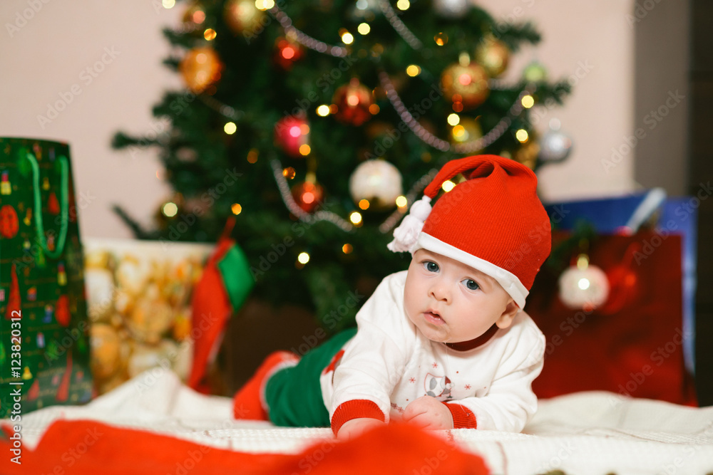 Christmas baby in hat holding red ball near gift box and new year fir tree Christmas baby in hat holding red ball near gift box and new year fir tree