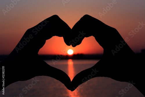 Silhouette of hands in form of heart on background of sunset.