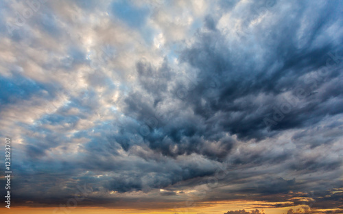 Beautiful dramatic sky with gray clouds and sunset. Dark blue feather shaped clouds in the background of bright orange sunset.