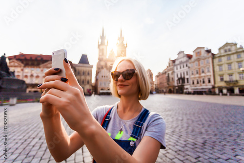 Beautiful young female traveler making self photo on her mobile phone on the background of the Church of Virgin Mary in Old Town Square in Prague. Kostel Panny Marie pred Tynem. photo