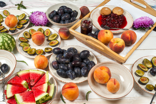 Colorful fruit set of purple  red and orange background in bowls. Plum  peaches  watermelon sliced above white tabletop