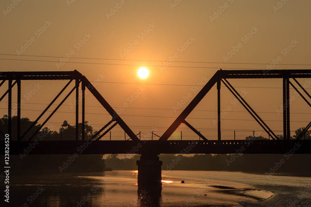 A backlit silhouette of a railroad tres-sel on a river at dawn