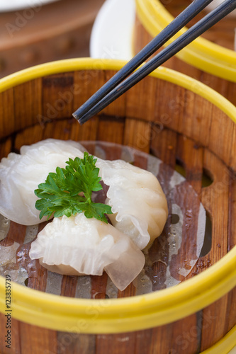 Chinese steamed white dumpling or Hakau Dim sum stuffed with minced shrimp decorated in bamboo made steamer local style with chopsticks. photo